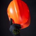 Orange construction helmet close-up. The man makes a greeting gesture with an orange construction helmet. A gloved hand raises the helmet above his head